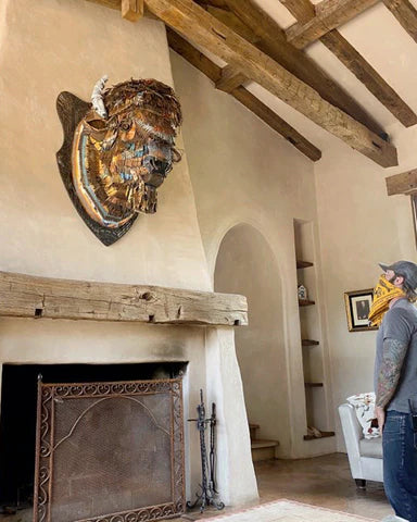 Large-scale bison taxidermy mount metal wall sculpture with metal backplate hanging above a fireplace with the artist Dolan Geiman